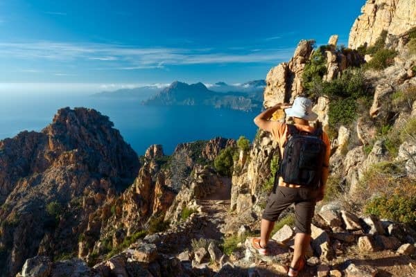 Wanderer mit Rucksack und Hut in der Bergregion Calanques de Piana auf Korsika