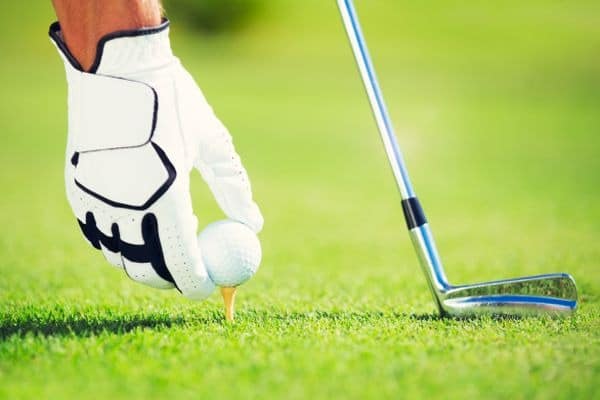 Hand eines Golfers mit weißem Handschuh, Golfball und Golfschläger