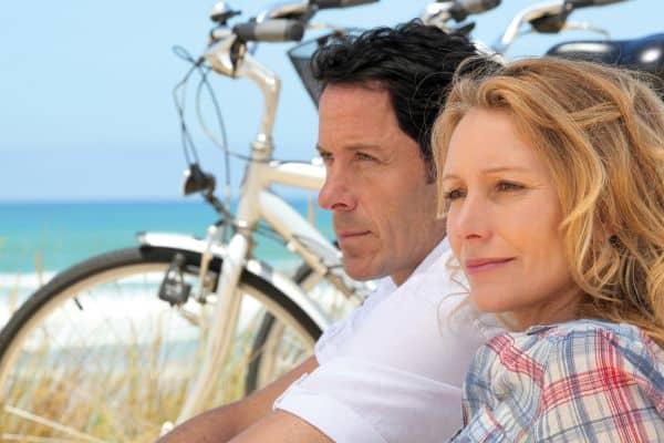 Paar sitzend im Sand mit abgestelltem Fahrrad und im Hintergrund das türkisblaue Meer
