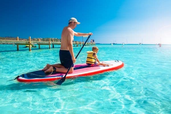 Vater und Sohn auf einem Stand-up-Paddle-Board im türkisblauen Wasser am Santa Giulia Beach auf Korsika