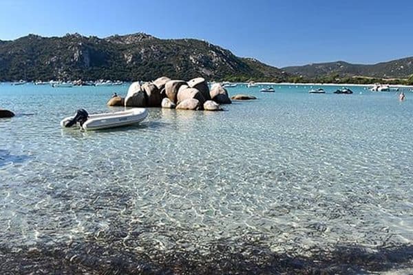 Traumhafter Strand von Santa Giulia auf Korsika mit Boot und Felsen im Wasser