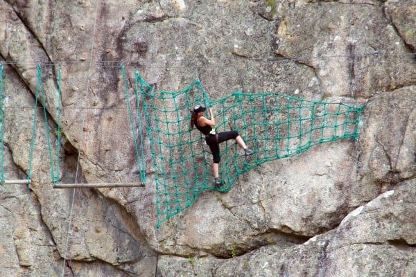 Frau klettert an einem grünen Netz an einer Felswand in der Region Solenzara auf Korsika