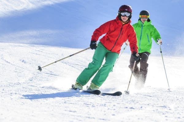 Zwei Personen in grüner und roter Skikleidung beim Skifahren